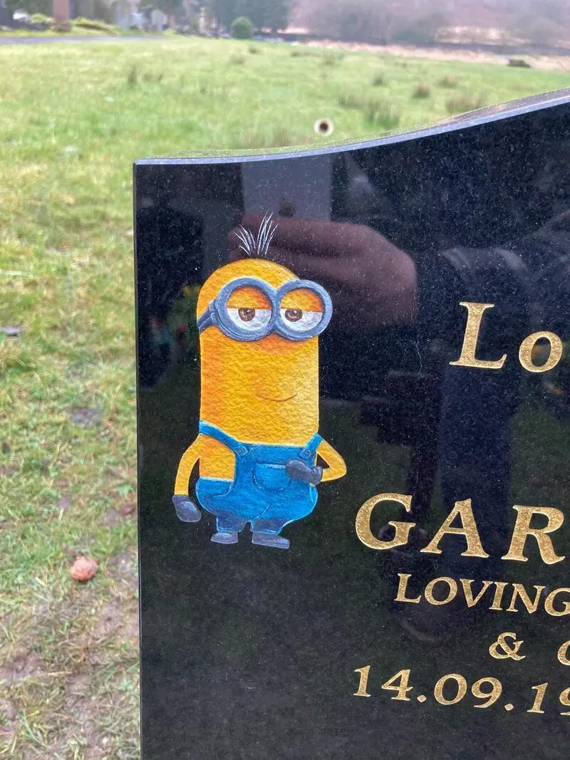 Black granite memorial with a full-colour hand-painted cartoon figure alongside gold leaf lettering by FR Terrazzo, Rhondda Cynon Taff